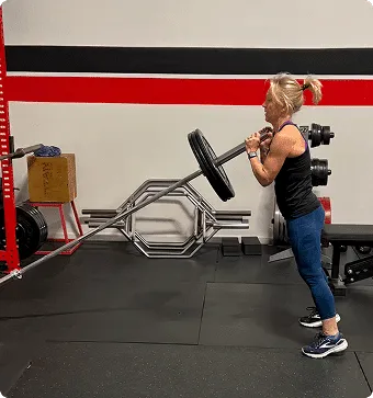 An adult woman in workout gear lifting a pole with a heavy weight on it at Rewire Health & Performance, performance training Franklin MA