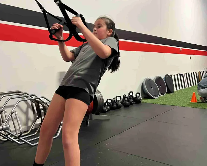 Young girl uses suspension straps at RHP Fitness Center for strength-based performance training and return from injury support